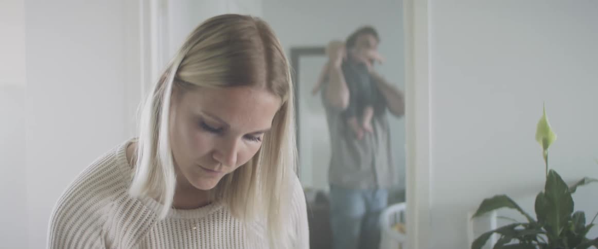 Father picks up and soothes child while mom works in another room