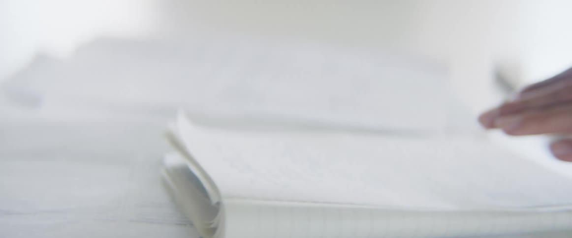 Womans hands write things down in a notebook and documents on a table