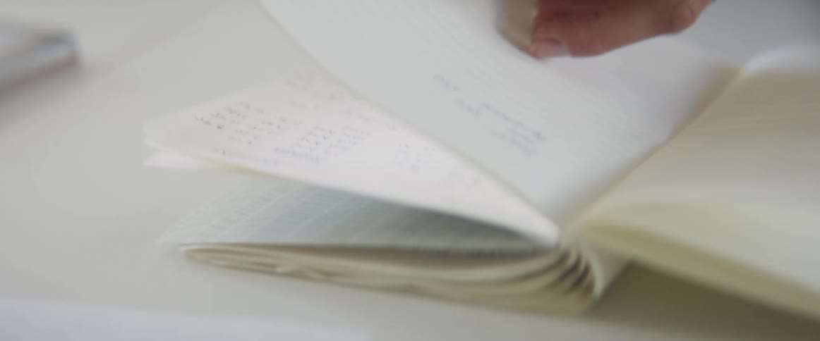 Womans hands leaf through a notebook on a table