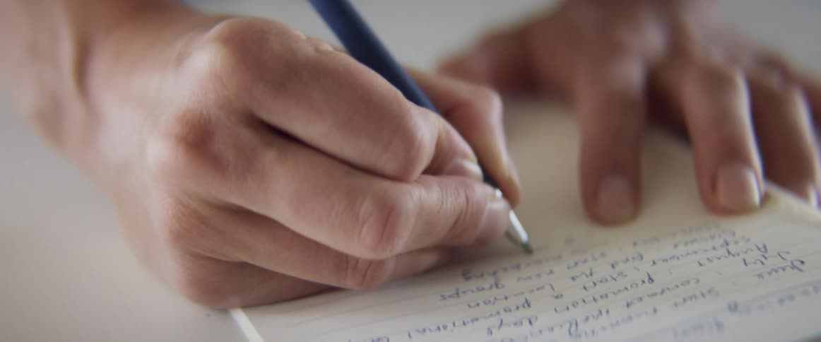 A woman quickly writes down notes on a yellow notepad