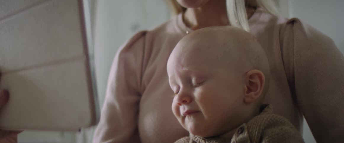 A woman looks at her tablet as she sits with her son in her lap