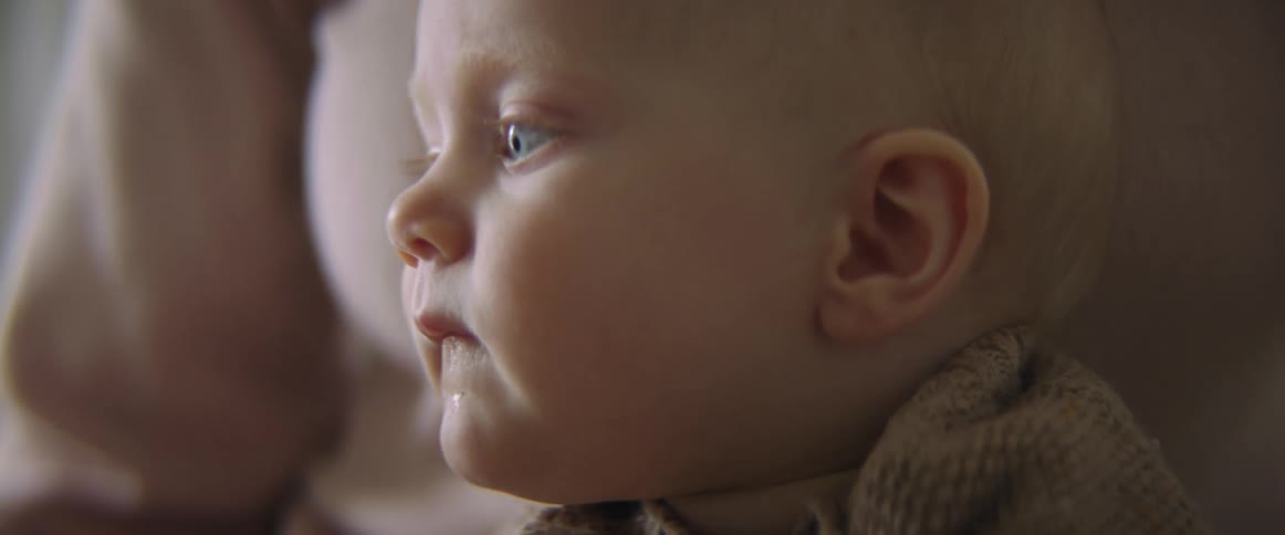 Blonde blue eyed baby sits in mothers lap as baby looks around