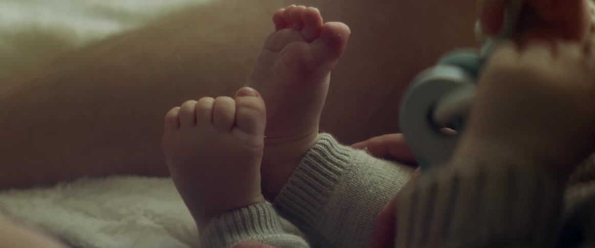 Baby touches his feets while playing with a toy sitting in a bed at home