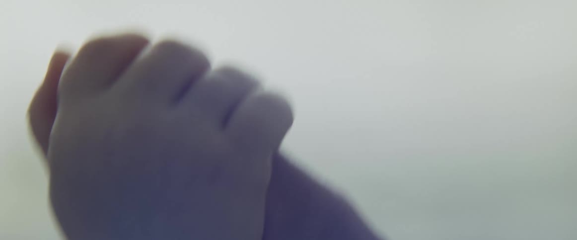 An adult allows a baby to play with their hand as sunlight shines in through the window