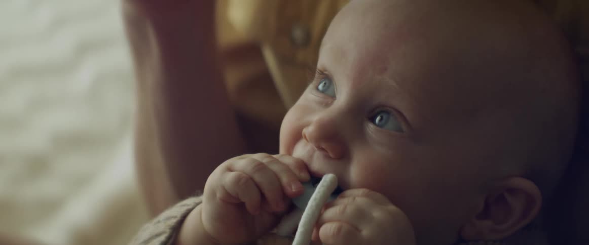 Baby boy chews on a toy in the lap of his mother at home