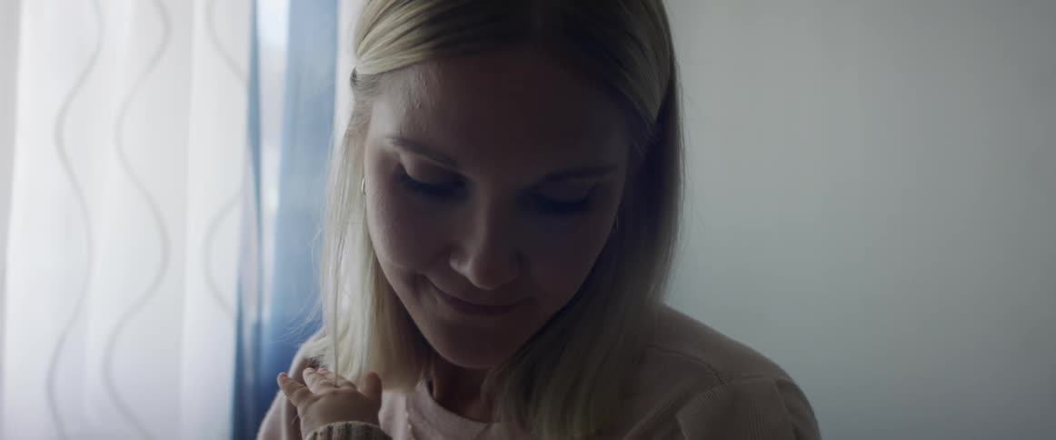 A white woman is holding her white son in her arms gently shushing him to sleep while he plays with her blonde hair