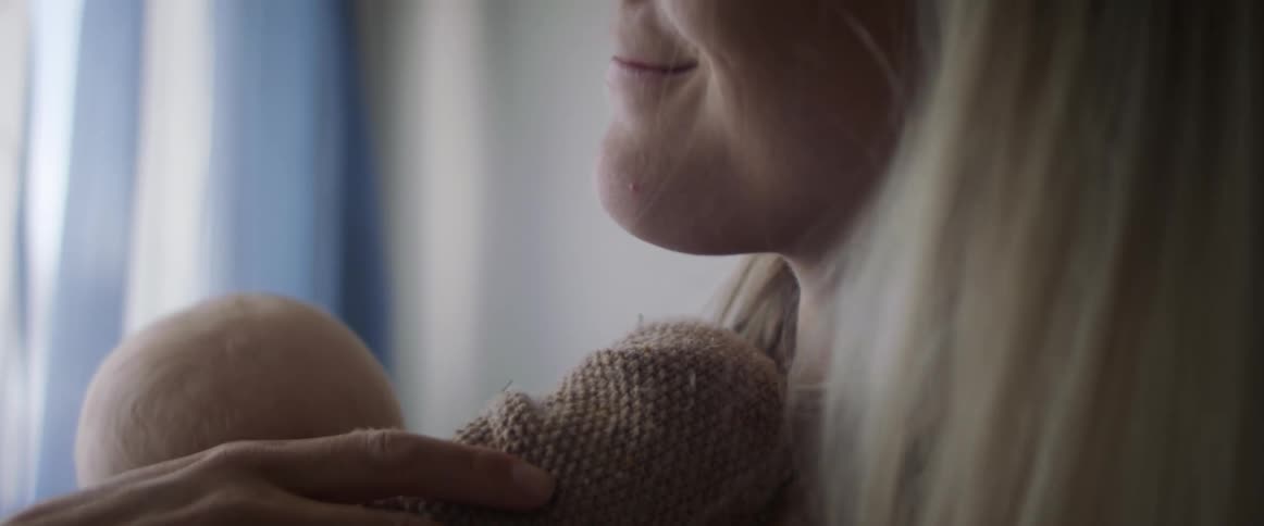 A woman smiles as she cradles a baby while standing near a window