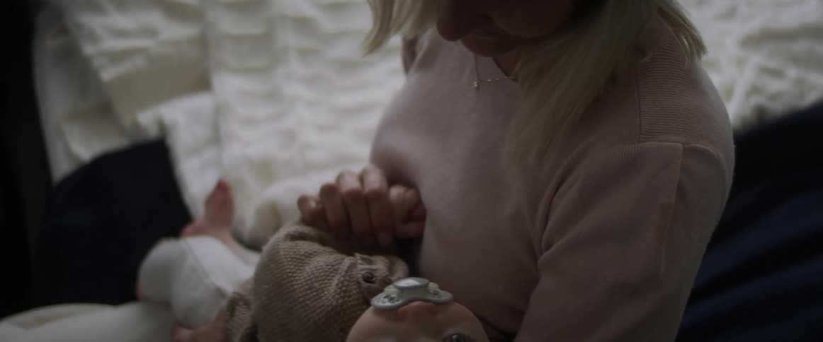 Blonde mother with a pink sweater holds her baby son sucking a rubber nipple