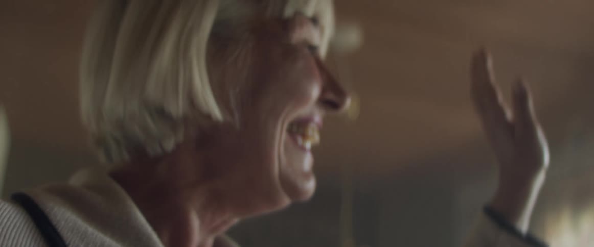 Senior woman smiles while wavingat someone from the living room at home