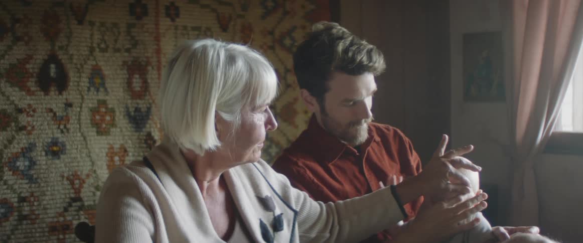 A grandmother rubs her grandsons son who is sitting in his dads lap