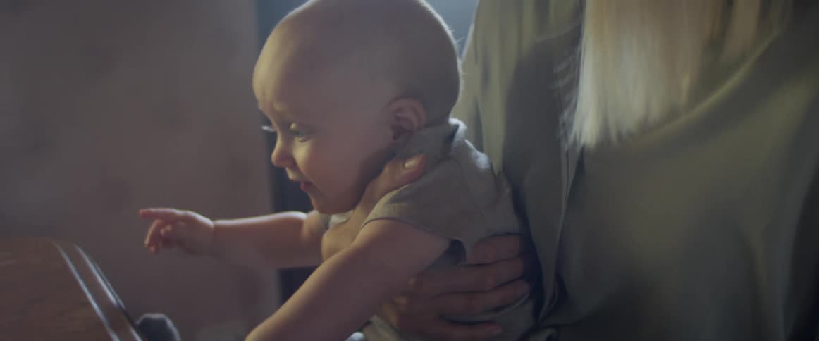 An infant boy sits on his mothers lap near a piano