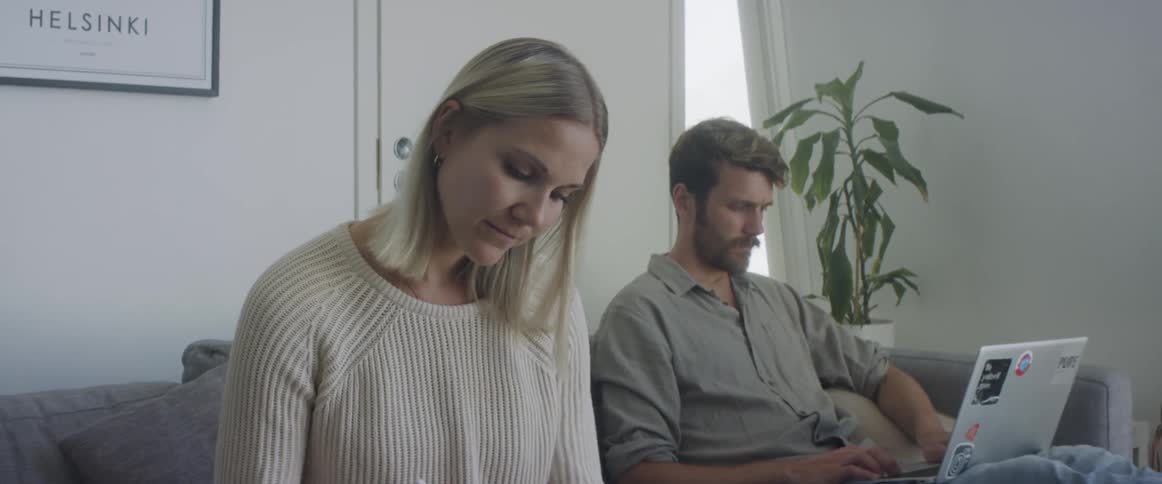 A man and woman sit on a couch beside each other with electronics