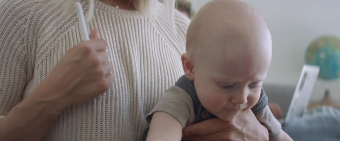 A mother holding her baby in her lap stops him from putting a pen in his mouth