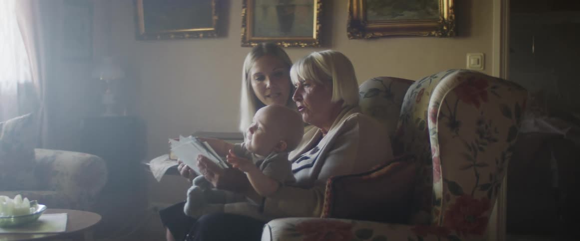 A middle aged woman holds a baby in her lap as she looks as photographs with a younger woman sitting beside her