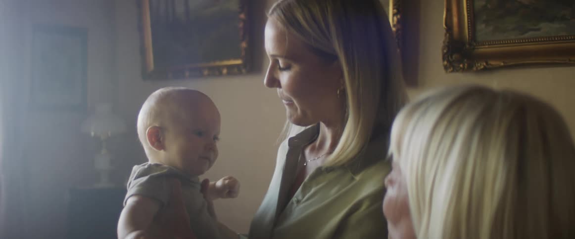 A woman lifts her baby up as her mom looks at them and smiles