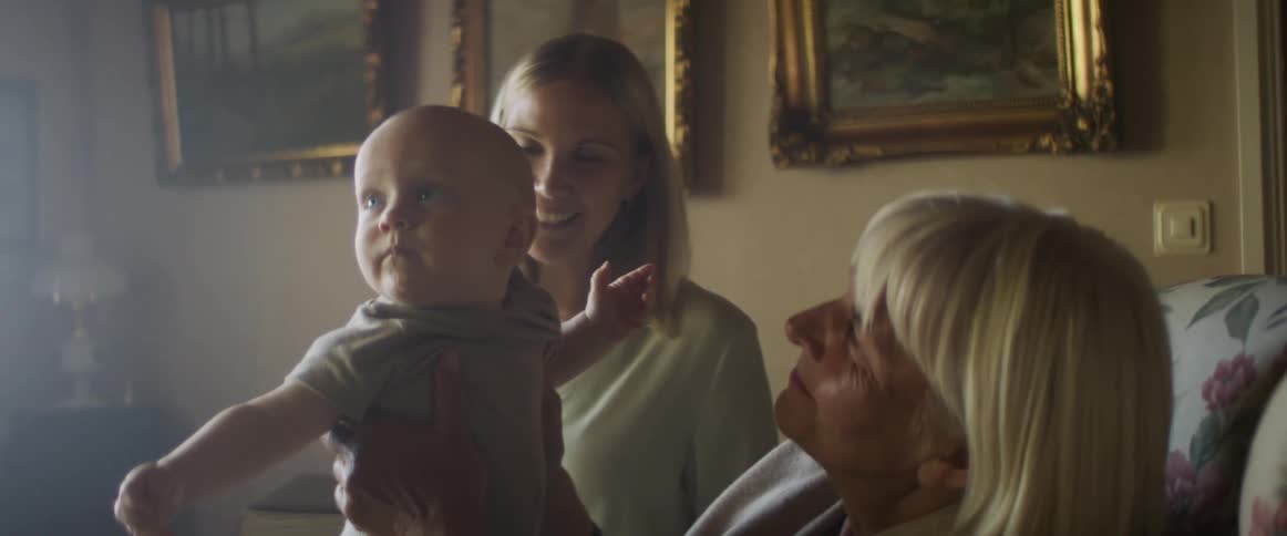 Grandmother plays with her grandson on the couch in the living room while the mother smiles