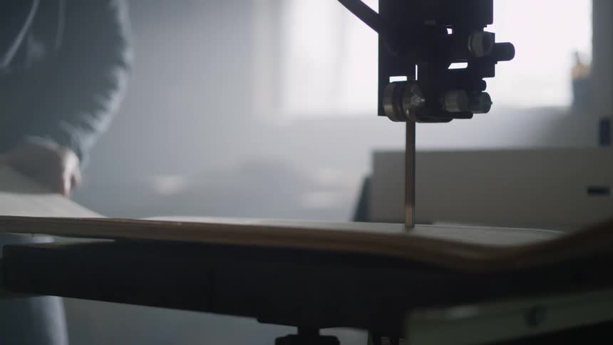 A man pushes a piece of wood through a table saw while working indoors