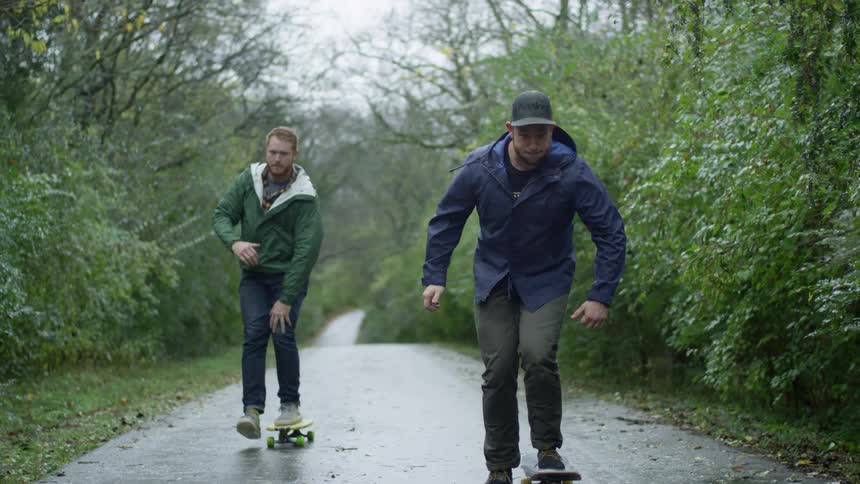 Men skateboard along highway through woulds wearing jackets