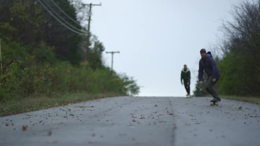 Two men skateboarding down a hill