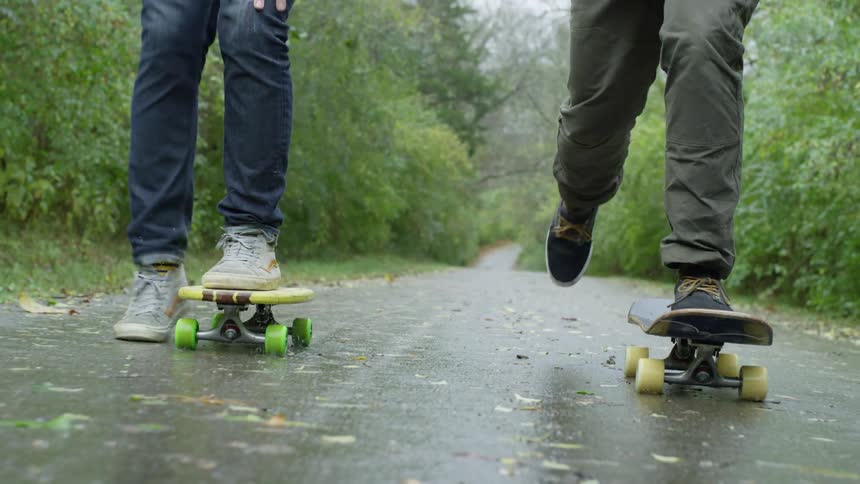 Two people skateboard on the slippery wet road