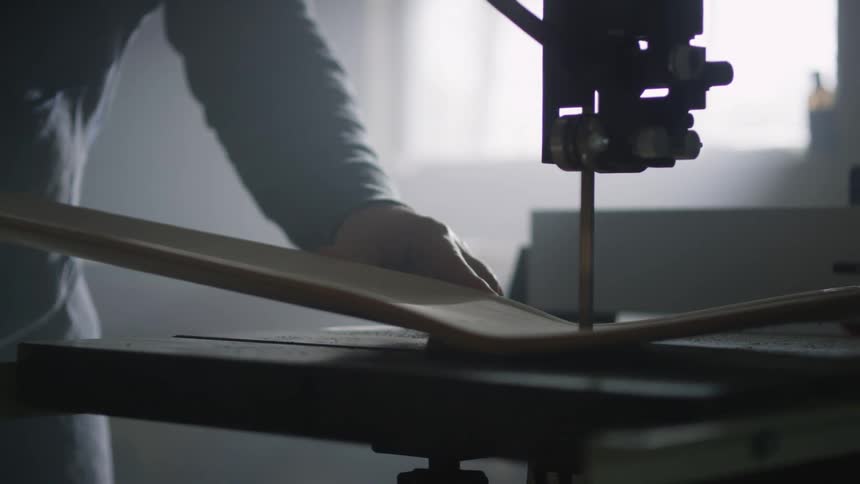 A person using an electric saw bench to cut wood inside a dimly lit workshop