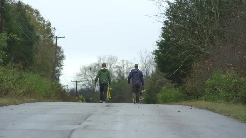 Two men walking down a street carrying skateboards