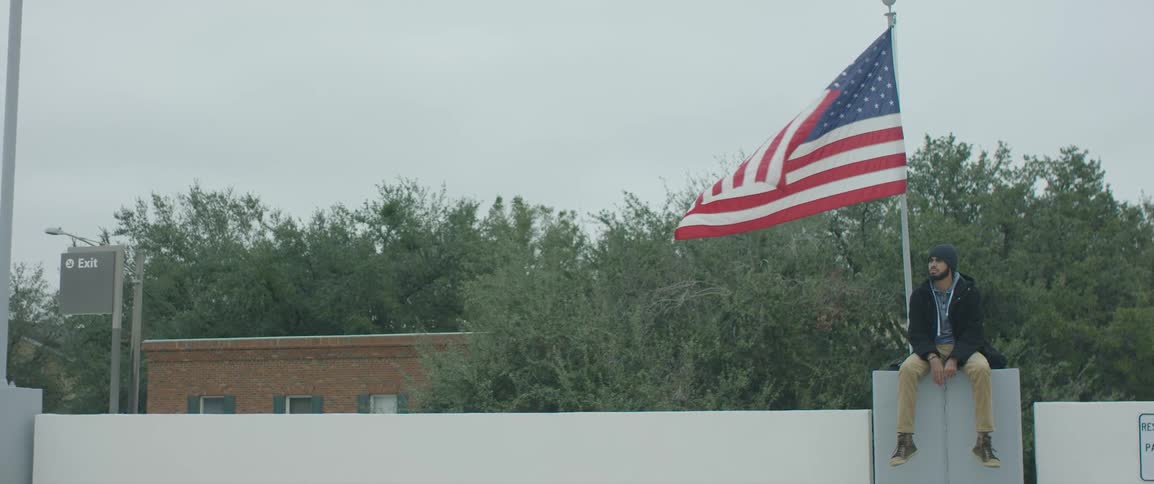 Man sits on cabinet on building near american flag