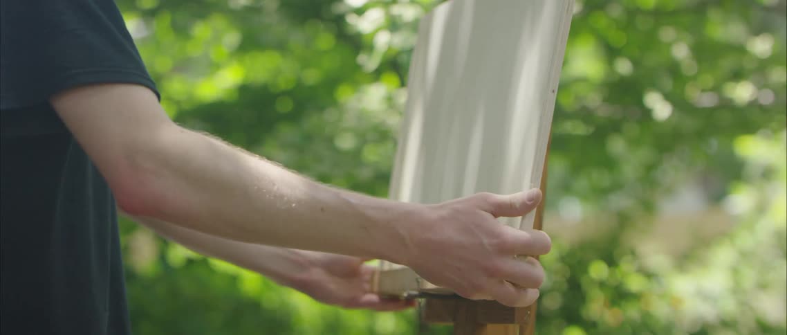 A person placing a canvas on a platform with plants and trees in the background