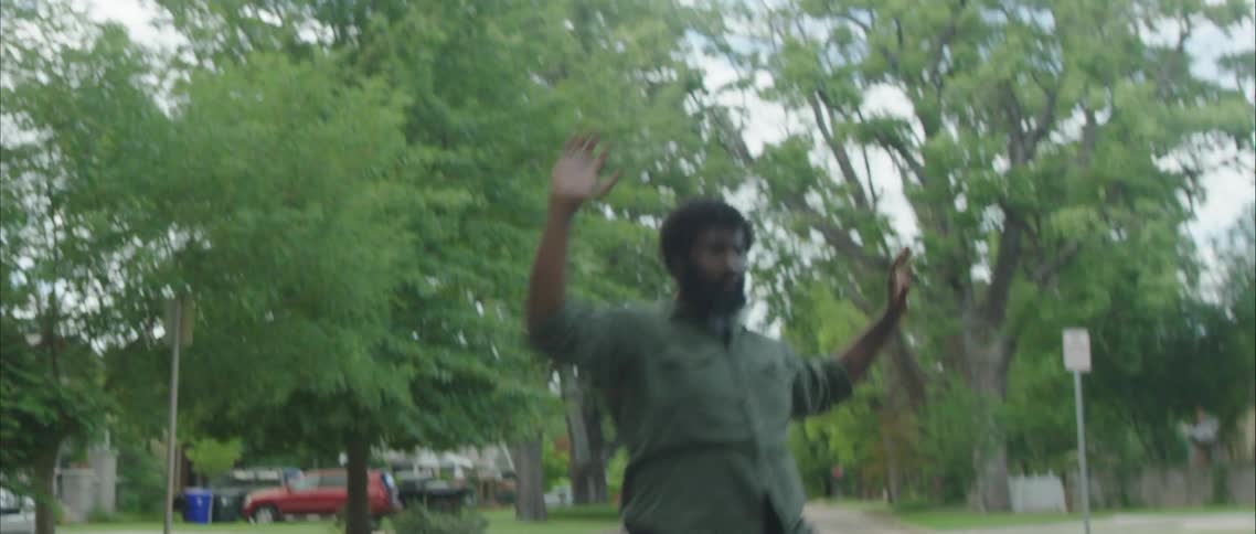 A black man dances in the middle of a street through a residential neighborhood during the day
