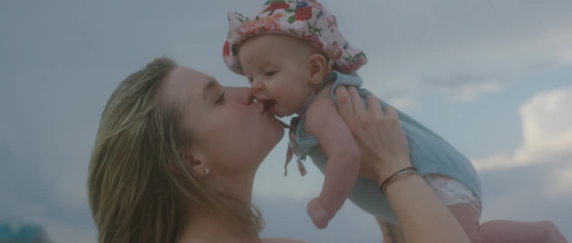 A woman holds her baby daughter and gives her a kiss as they stand on the beach
