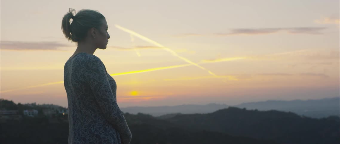 A woman standing and overlooking mountains at sunset