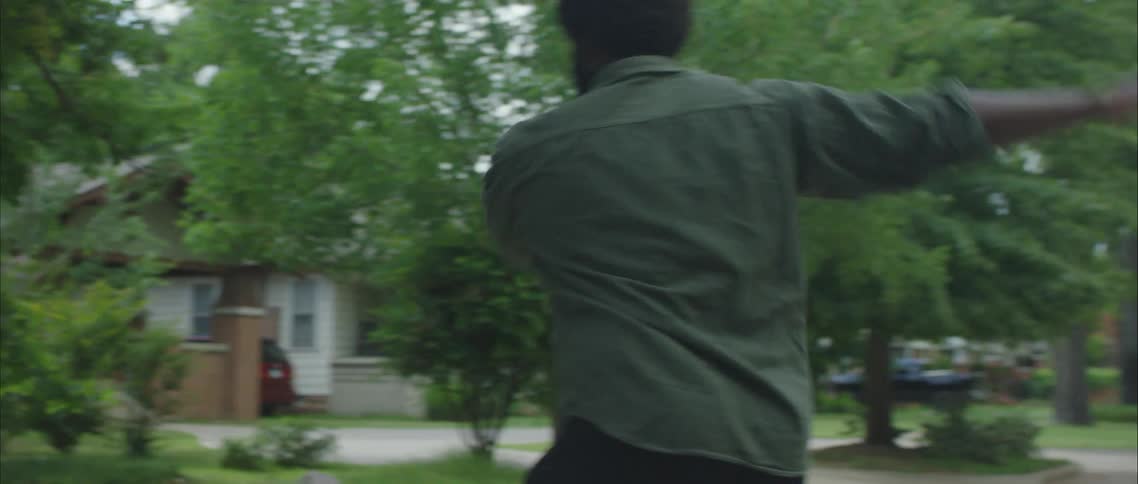 A black man dances in the street of a residential neighborhood during the day