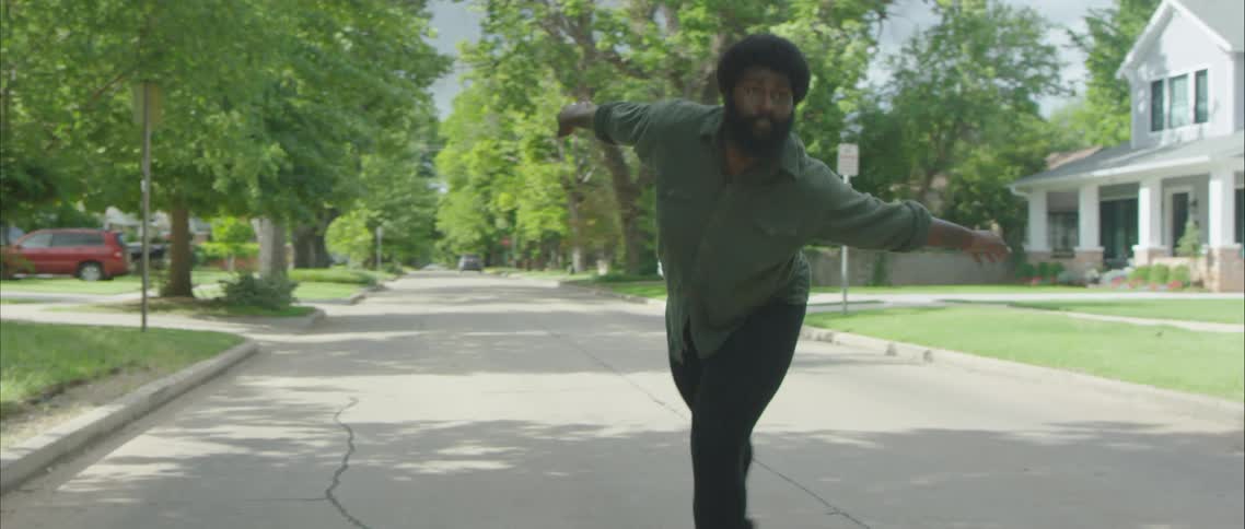 A man dancing on a residential street on a summer day