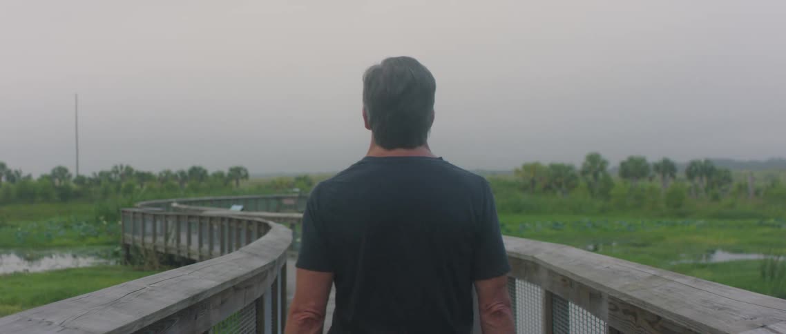 A man walking on a rural wood walkway on a summer day