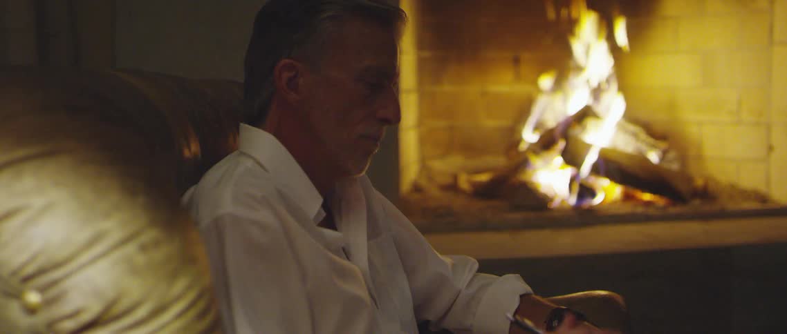 A man writing in a notebook while sitting next to a burning fire in a fireplace