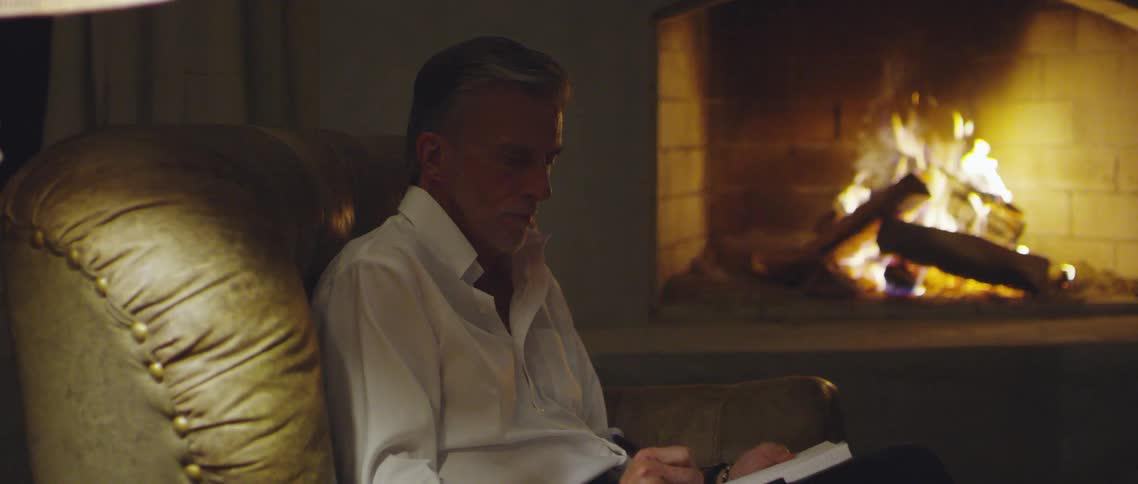 A man sits in a leather armchair by his fireplace and writes in a blank notebook