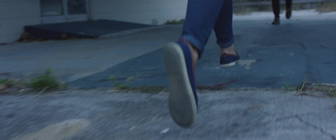 Person runs across pavement outside past a building to another person who is walking