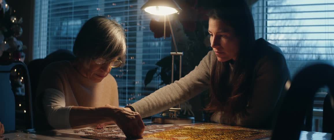 A woman sits with her elderly mother putting together a jigsaw puzzle at christmas time