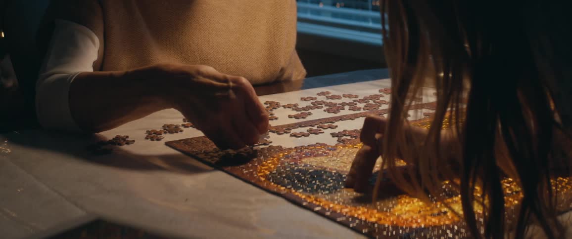 A woman works on a jigsaw puzzle with her daughter and granddaughter near their christmas tree