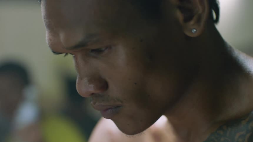 A bare chested man stands inside and looks down at his tattoos