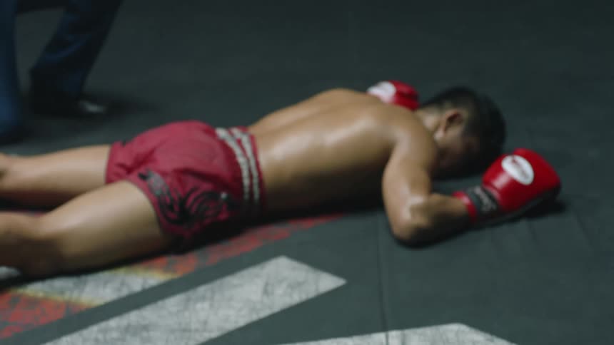 Boxers in a ring with a referee and one boxer is knocked out to the floor of the ring
