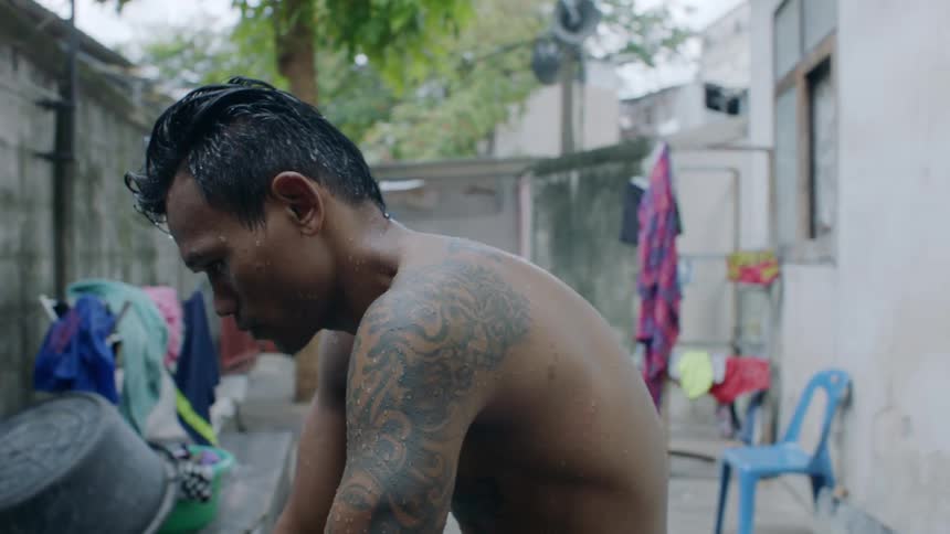 A shirtless man sits on his patio staring at a wall before putting his head down