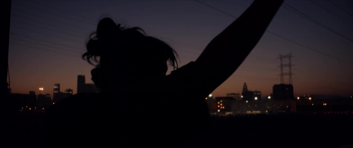 A woman waves her arms around and spins as she dances outside in front of a city skyline