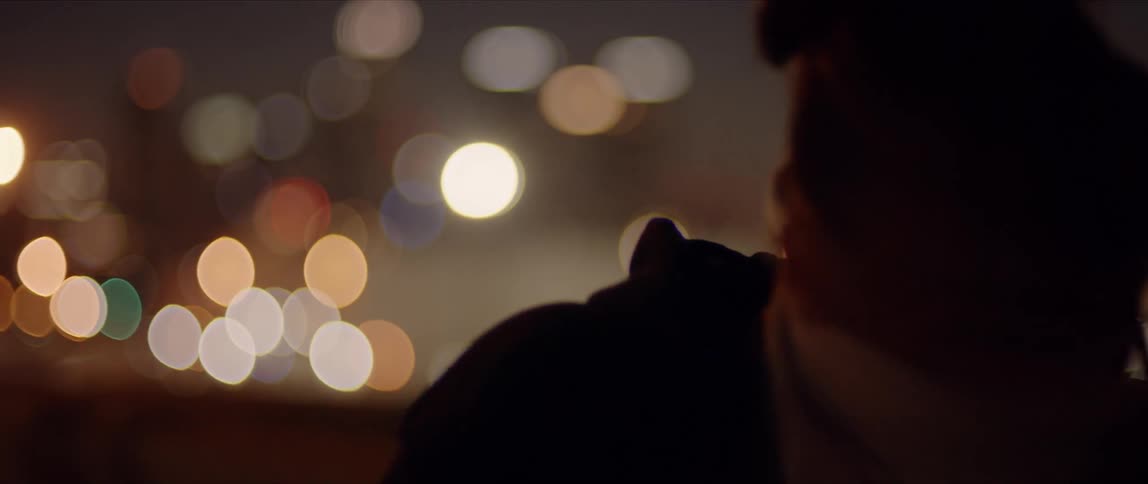 A woman wearing a bandana that covers the bottom of her face dances on top of a city building at night