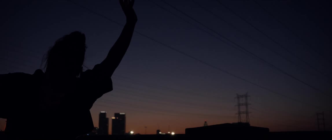 Silhouette of woman moves and sways under power lines with city skyline in background