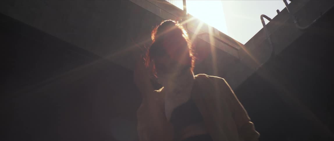 Bright sunlight shines down on a woman dancing outside a building