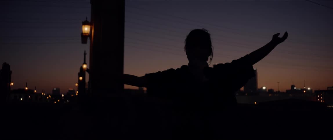 Silhouette of a woman posing and dancing in front of a city skyline at sunset