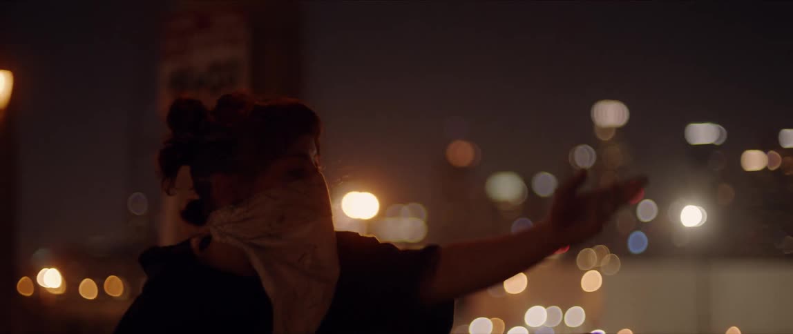 Dancer wearing bandana as mask dances with blurry city lights in background