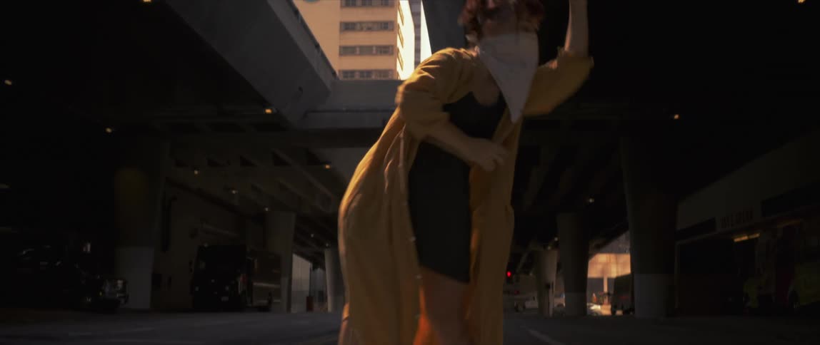 Young woman wearing a yellow robe and face mask dancing in the street of a city