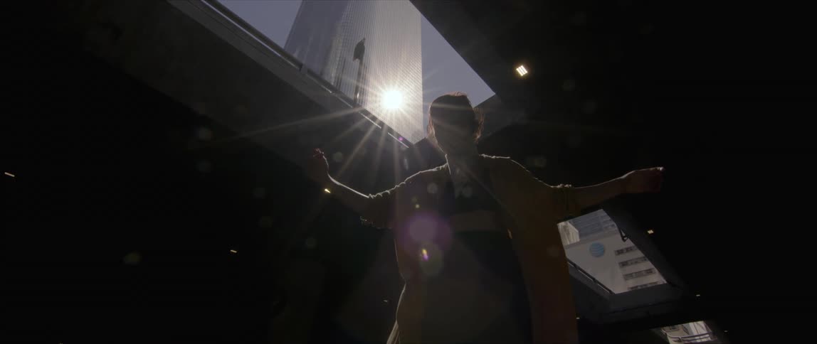 A woman dancing with buildings the sky and clouds and sunlight in the background